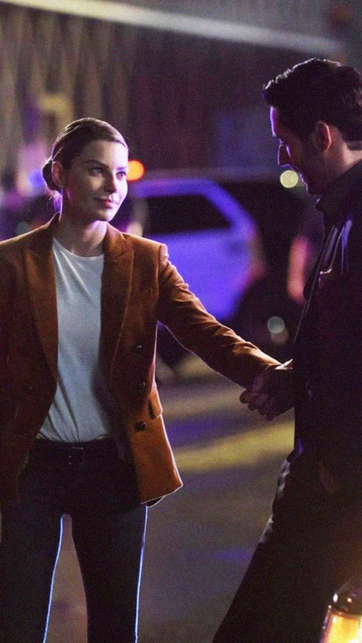 a man and woman holding hands walking down the street at night with cars in the background