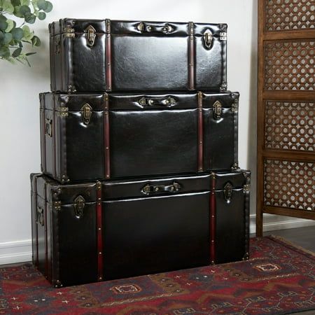 three black trunks stacked on top of each other in front of a rug and plant