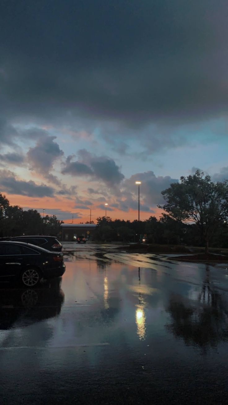 cars parked on the side of a wet road at night with clouds in the sky