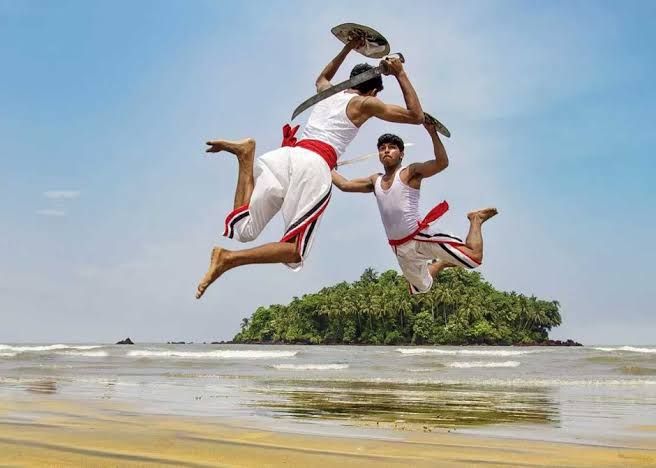 two men jumping in the air while holding onto each other's legs on a beach