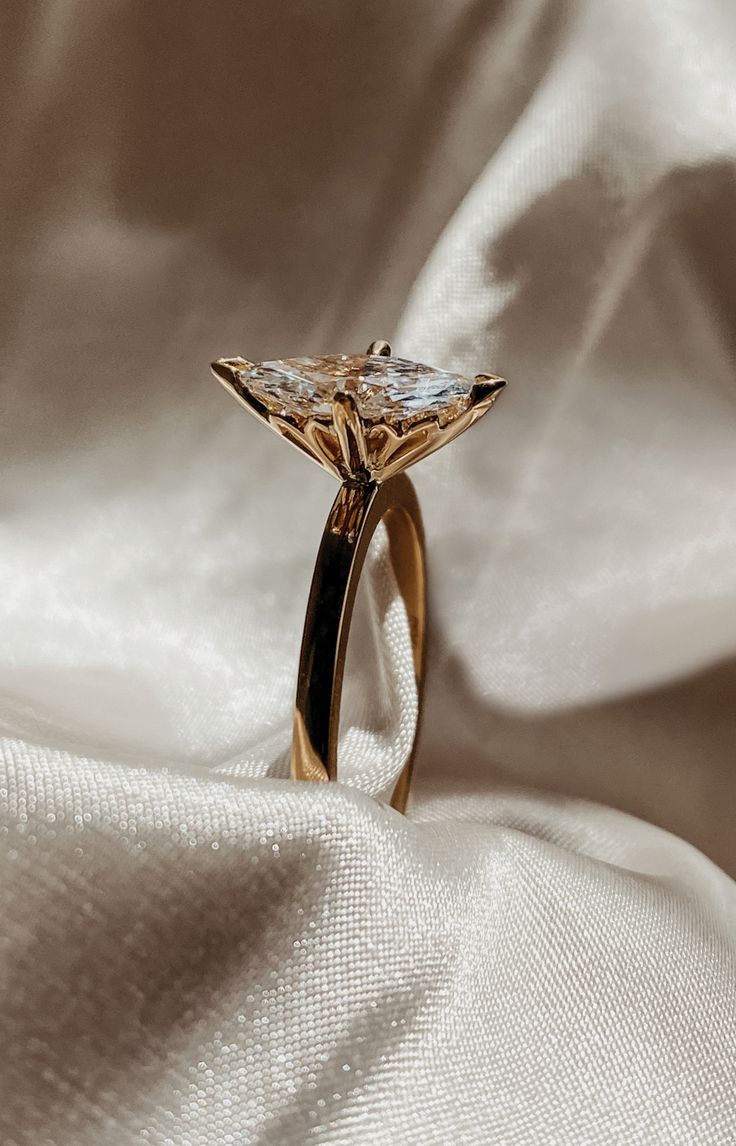 a gold ring with a diamond on it sitting on a white cloth covered tablecloth