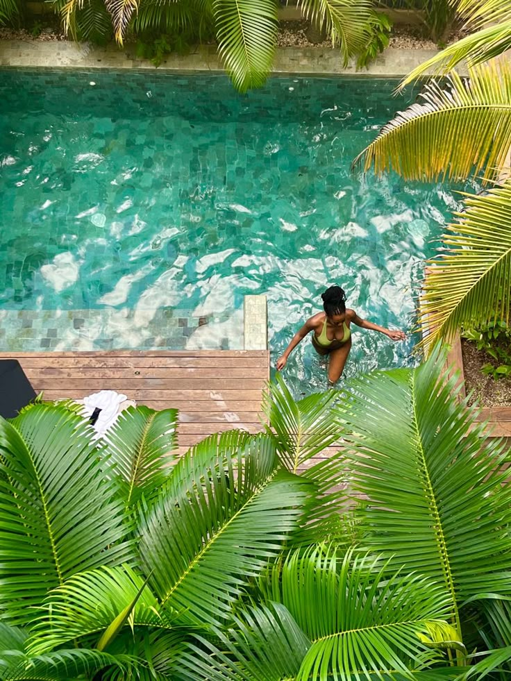 a woman is swimming in a pool surrounded by palm trees and other greenery,