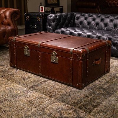 a brown leather trunk sitting on top of a carpeted floor next to a couch