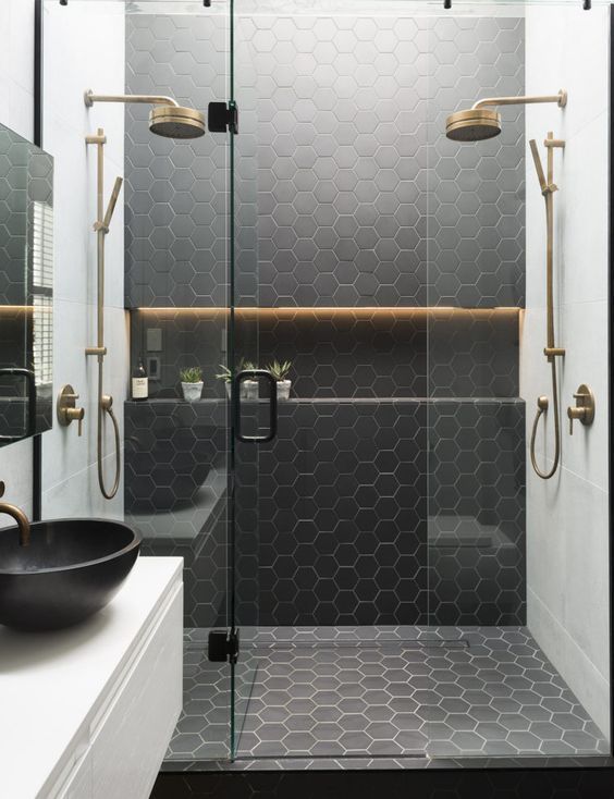 a black and white bathroom with hexagonal tiles on the walls, an oval sink and a glass shower door