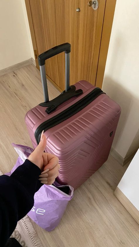 a person holding onto a piece of luggage in front of a door with a purple bag on the floor