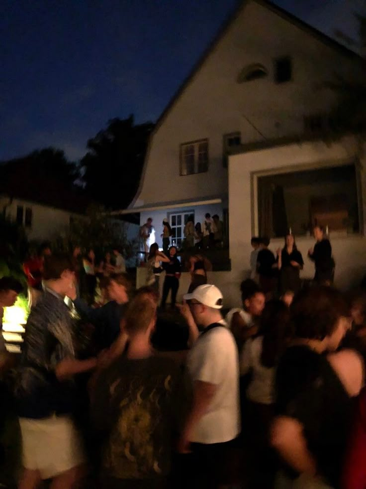 a group of people standing in front of a house at night with their cell phones up