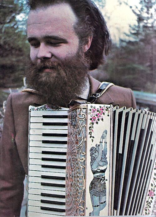 a bearded man holding an accordion in front of his face