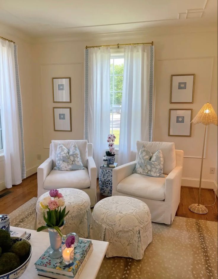 a living room with two white chairs and a coffee table in front of the window