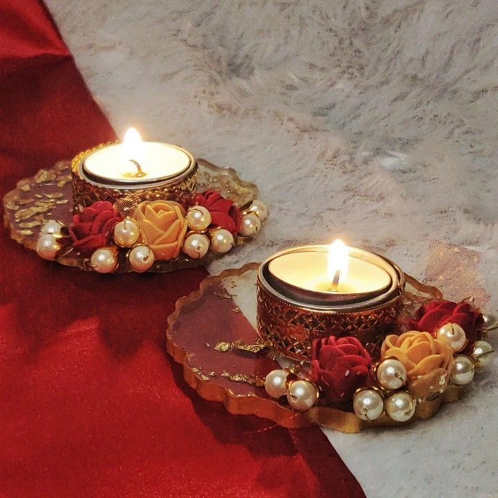 two candles are sitting on a red table cloth with flowers and pearls around them,