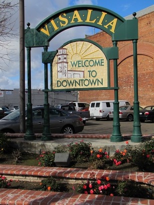 a welcome sign to downtown with cars parked in the parking lot and brick steps leading up to it