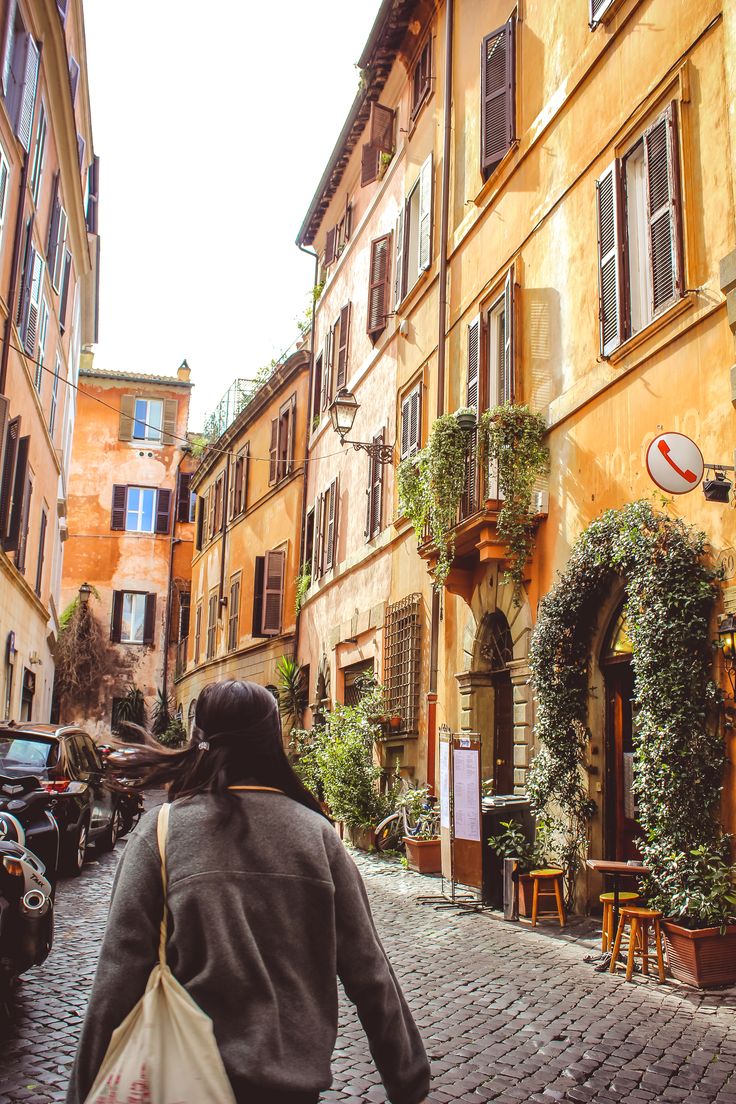 a woman walking down a cobblestone street in an old european city with tall buildings