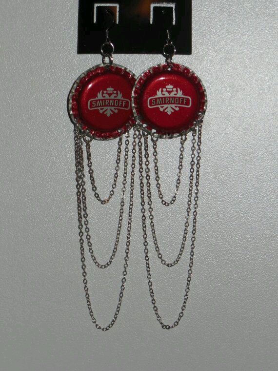 two red bottle caps with chains hanging from the wall next to a pair of earrings