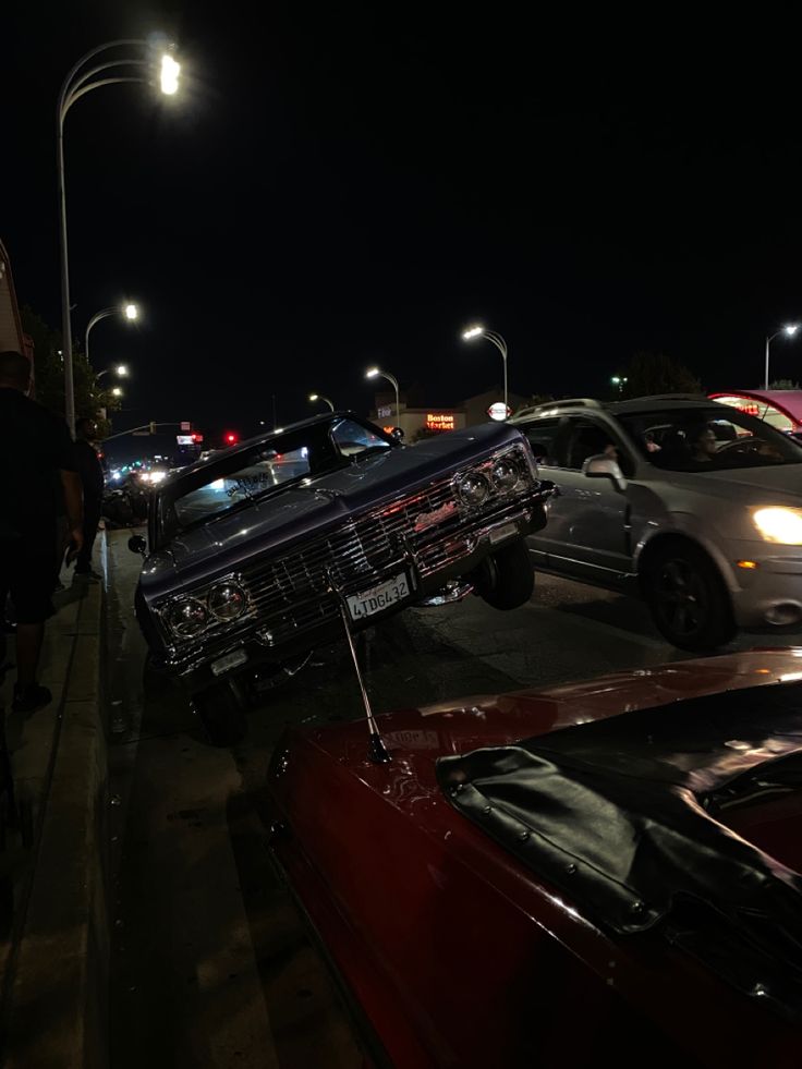 several cars are parked on the side of the road at night with street lights in the background