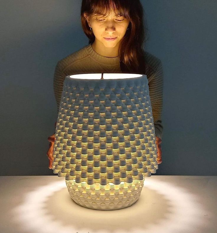 a woman is holding a lit up vase with circles on it and the light reflecting off her face