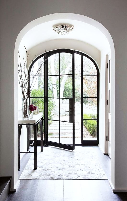 an arched doorway leading to a foyer with black doors and white rugs on the floor