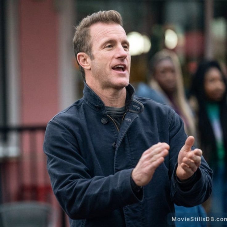 a man standing in front of a group of people talking to each other on the street