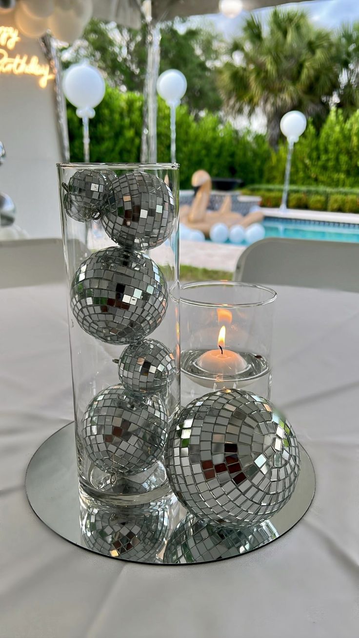 a glass vase filled with lots of disco balls on top of a table next to a pool