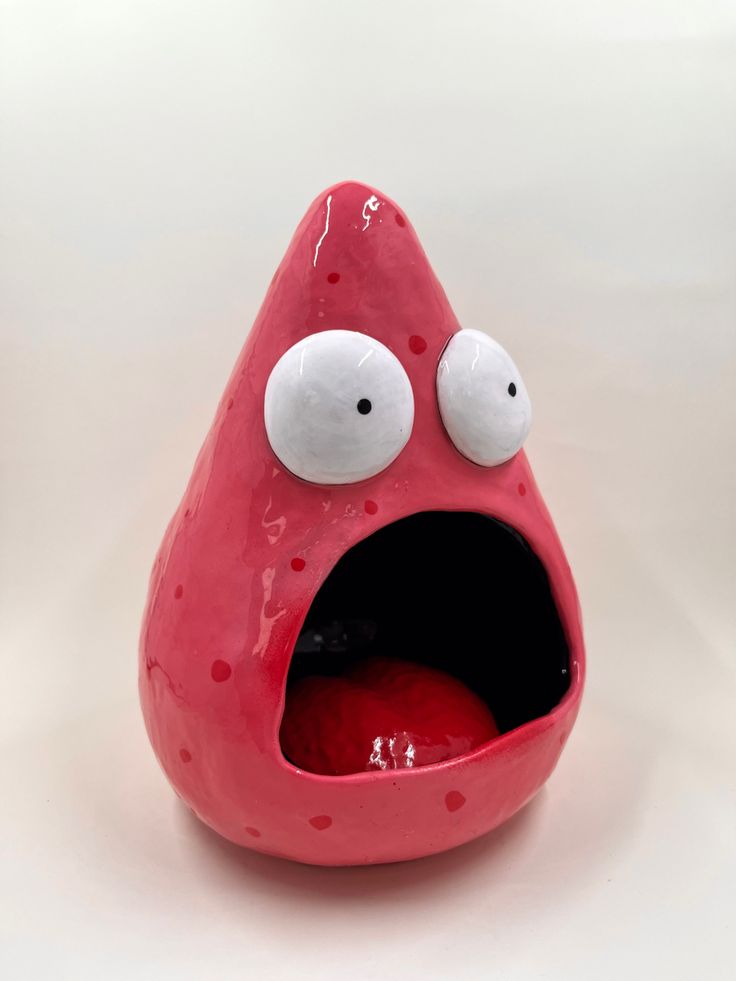 a red object with eyes and mouth on a white surface, showing its tongue out