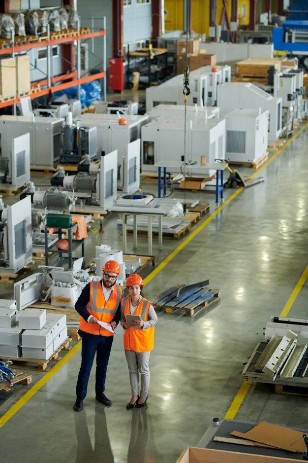 two men in orange vests and hard hats standing next to each other on a factory floor