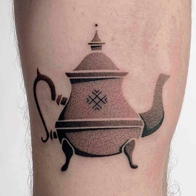 a black and grey teapot tattoo on the right leg with an arrow in it