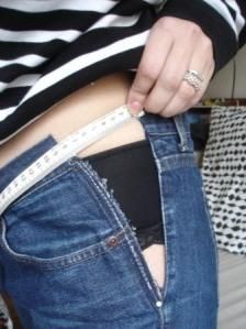 a woman is measuring her waist with a tape and wearing a pair of blue jeans