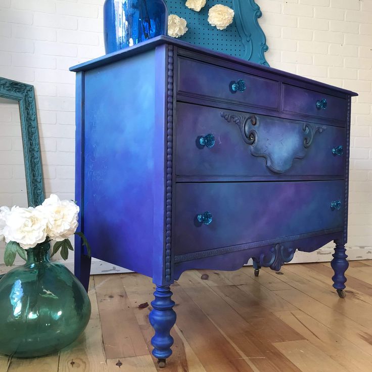 a blue dresser sitting on top of a wooden floor next to a vase with flowers