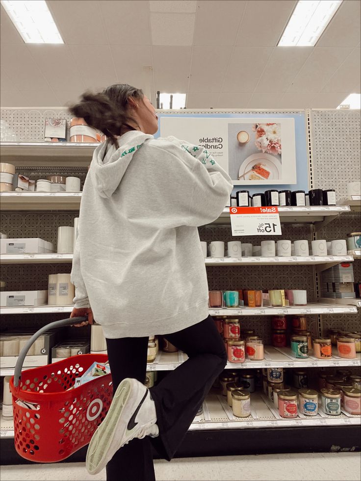 a woman is walking through a store aisle with a shopping basket in her hand and she's looking at the shelves