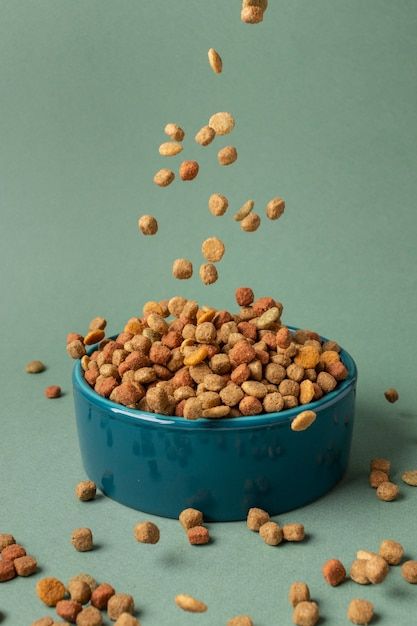 a blue bowl filled with cat food on top of a table next to a green wall