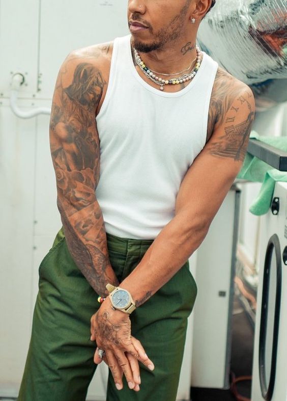 a man with tattoos standing in front of a washing machine wearing green pants and a white tank top