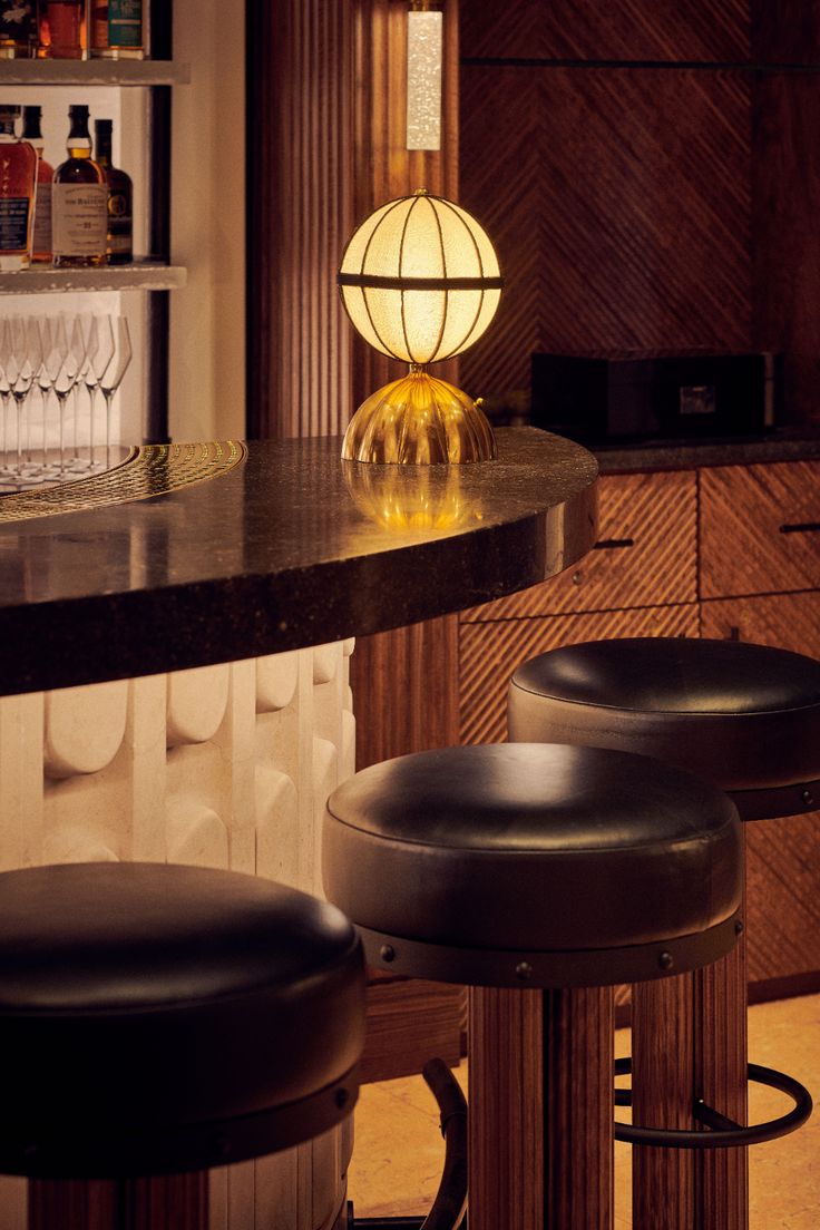 three stools in front of a bar with bottles and glasses on the shelves behind it