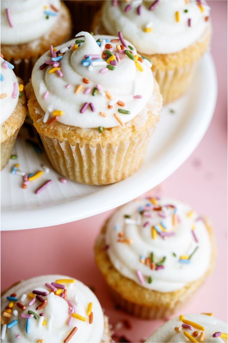 cupcakes with white frosting and sprinkles on plates