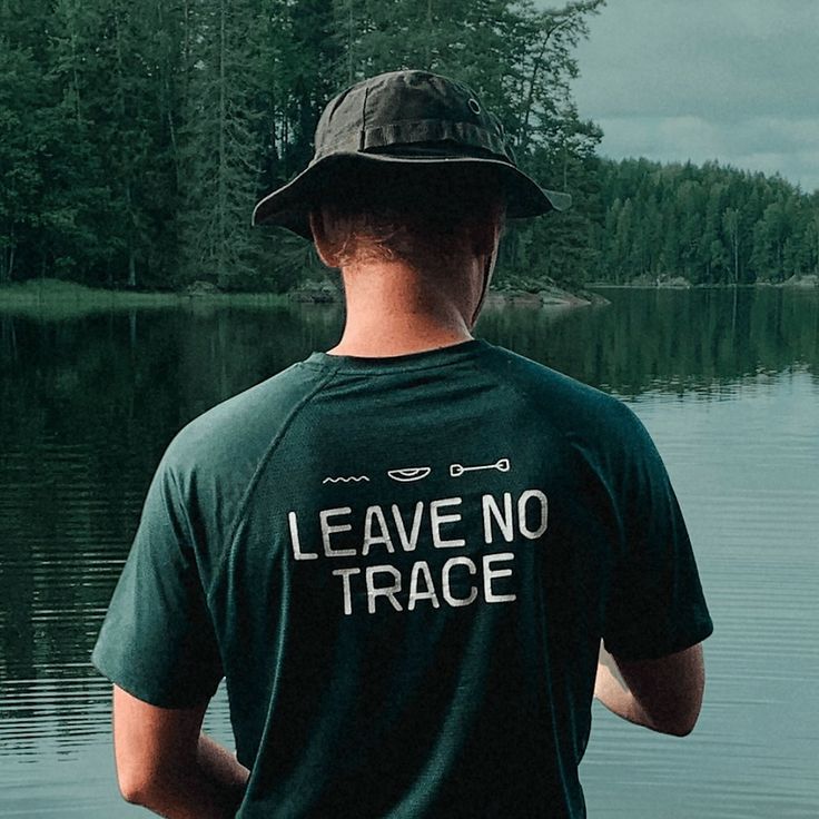 a man standing in front of a body of water wearing a shirt that says leave no trace