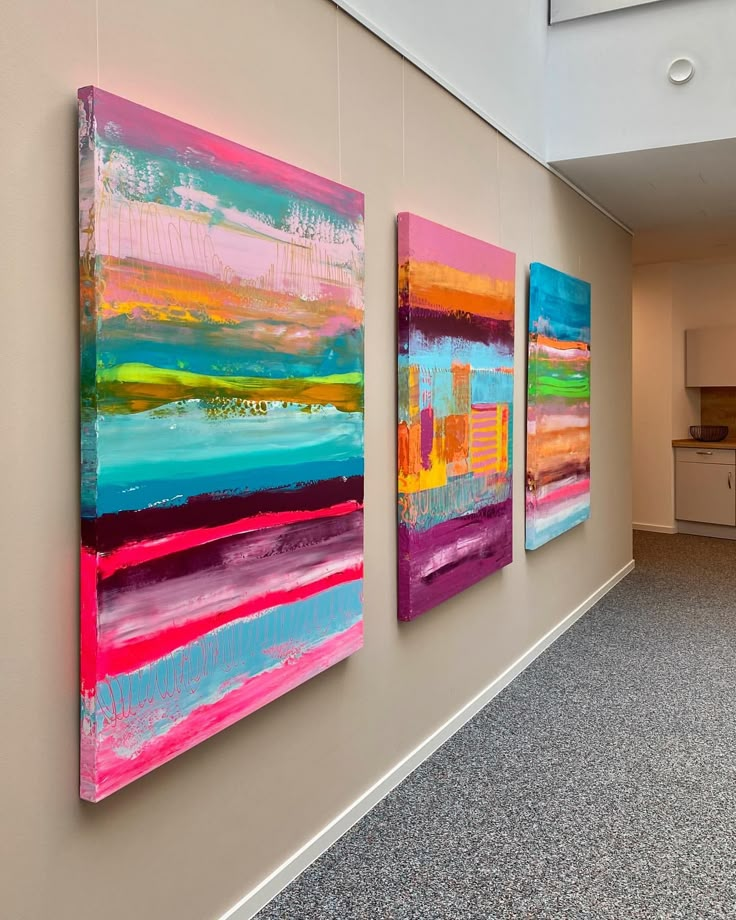 three colorful paintings are hanging on the wall in an empty room with carpeted flooring