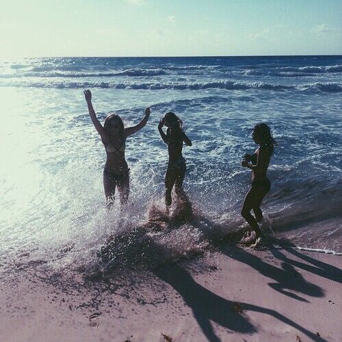 three women are running into the water at the beach, one is holding her arms in the air