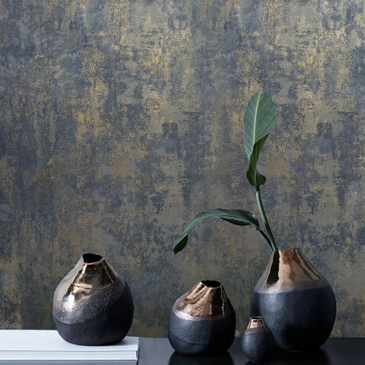 three black vases sitting on top of a table next to each other with a plant in them