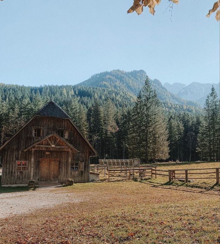 an old barn sits in the middle of a field with mountains in the back ground