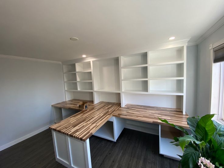 an empty room with white shelves and wooden counter tops in the center is a potted plant