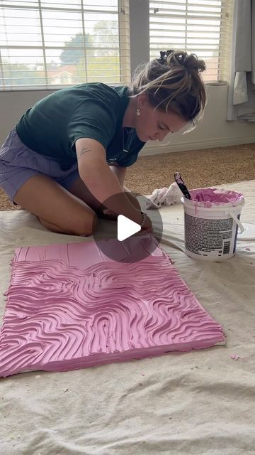 a woman is painting on the floor with pink paint and she is using a brush