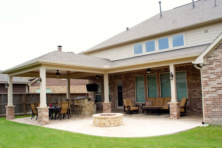 a patio with an outdoor fireplace and grill area in the middle of it, surrounded by grass