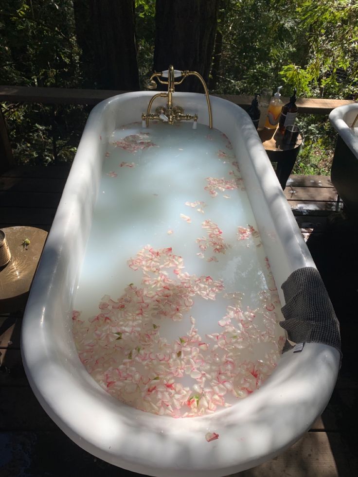 an old fashioned bathtub filled with water and pink flowers on the outside, next to a tree