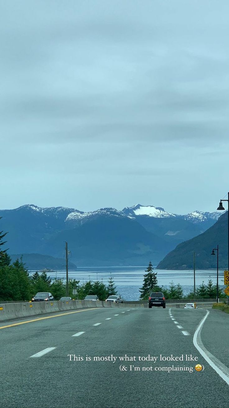 an empty road with mountains in the background and a car driving down the road on it