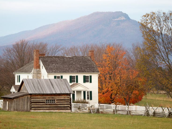 an old farm house with a mountain in the background and autumn foliage