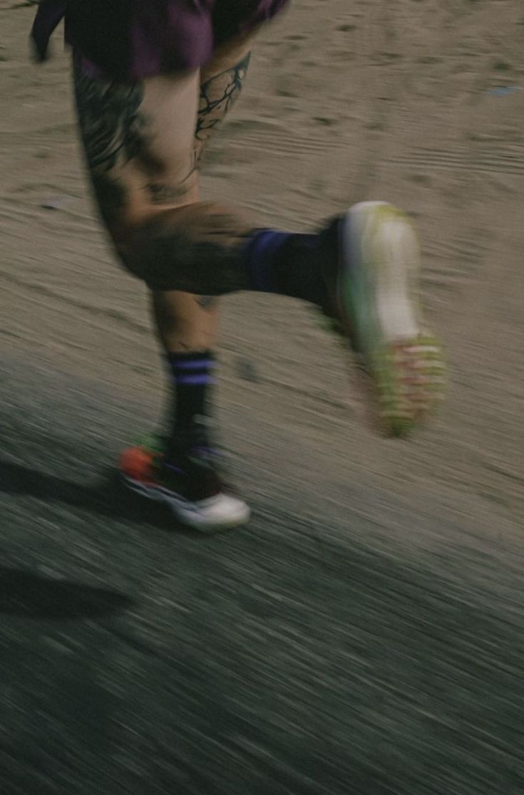 a man in purple shirt and shorts kicking a soccer ball on dirt field next to trees