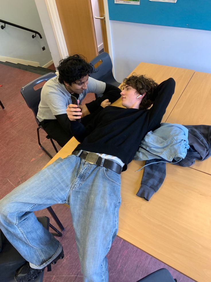 two young men sitting at a table with one laying on the floor and another standing