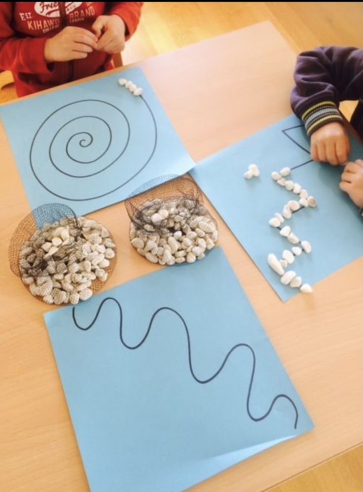 two children are sitting at a table making their own art project with blue paper and marshmallows