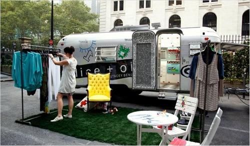 two people standing in front of an rv with clothes hanging on the rack and chairs