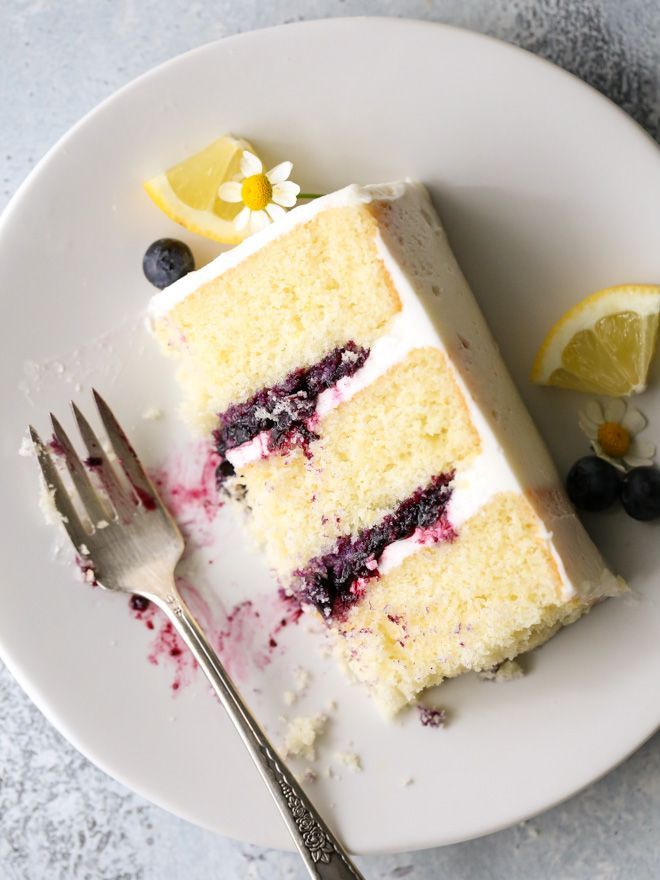 a piece of cake with blueberries and lemon on top sits on a white plate