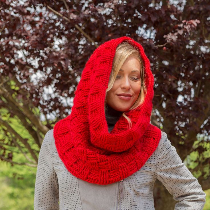 a woman wearing a red knitted cowl in front of a tree with her hands on her hips