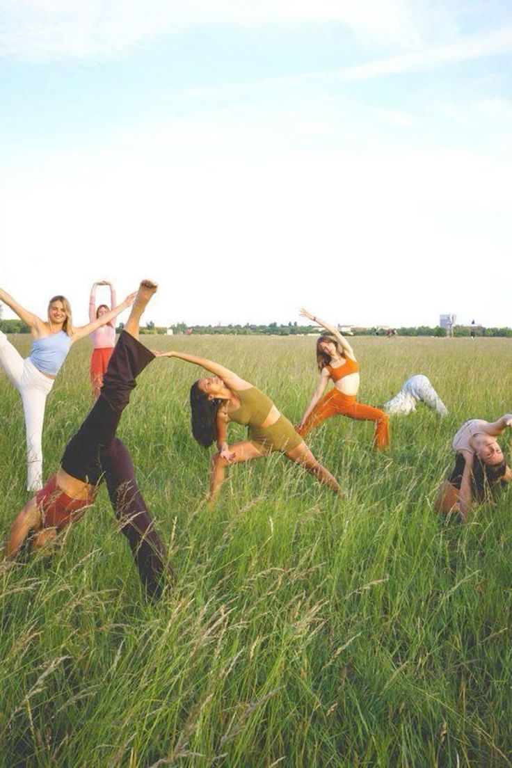 four people are doing yoga in the tall grass with their arms up and legs spread out