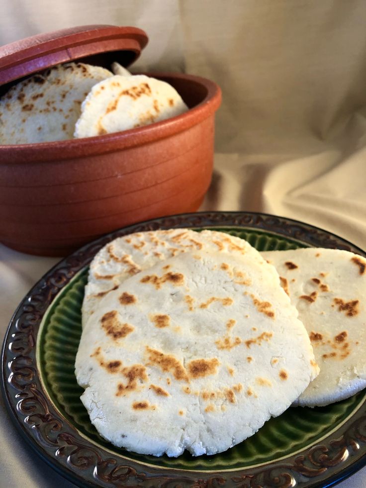 two flat breads on a green plate next to a potted plant and white cloth